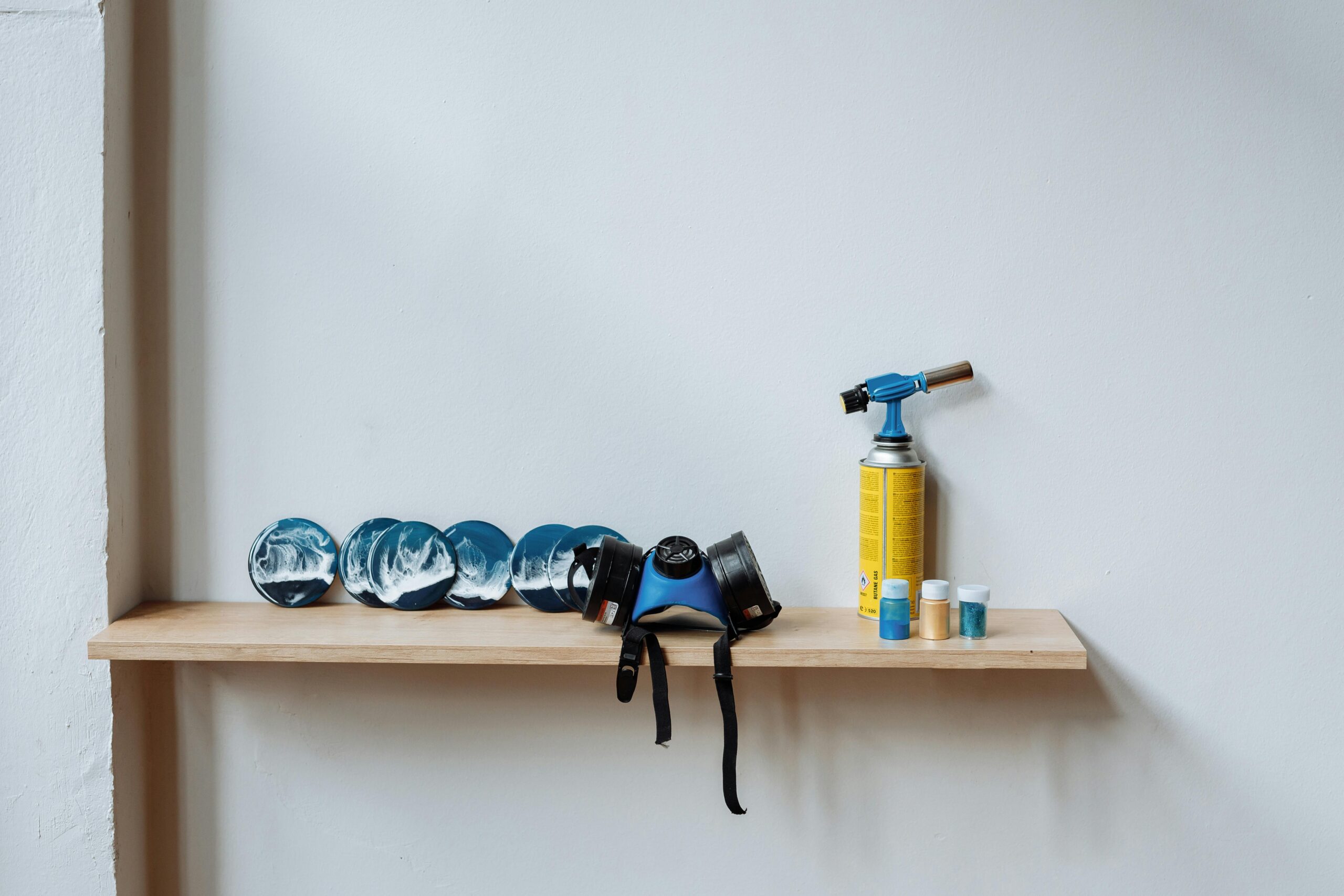 A wooden shelf displaying resin art, blow torch, and safety gear, illustrating a creative workspace.